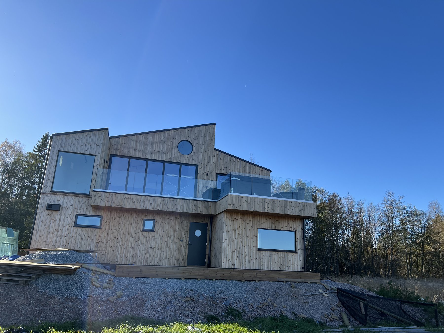Modernt hus med ljus träfasad och glasräcke på altanen